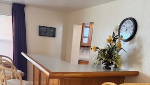 A bar area with a wooden counter, wicker chairs, a clock, and a potted plant.