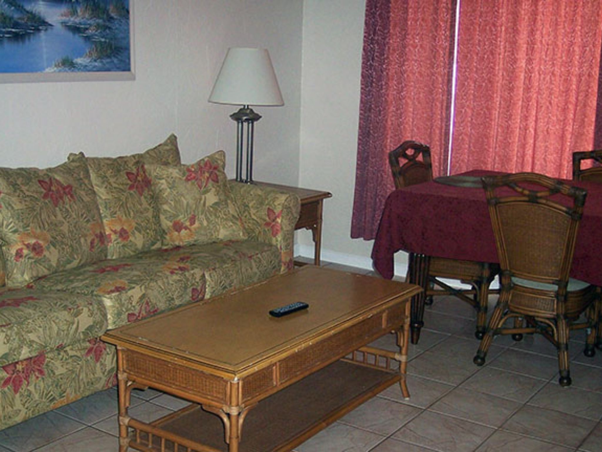 Ein Wohnzimmer mit einem blumigen Sofa, einem Holztisch, einem Esstisch mit Stühlen und einer Lampe.