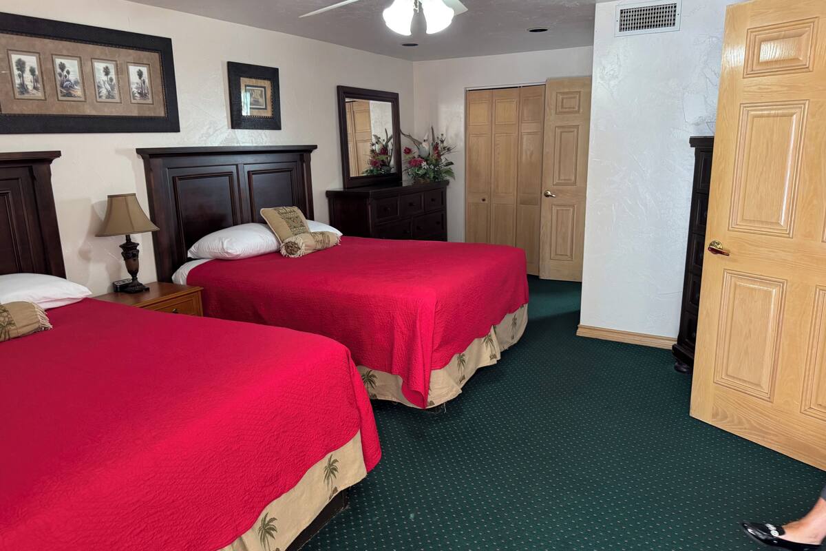 Habitación de hotel con dos camas, un ventilador de techo, un aparador, un espejo y una puerta de madera.