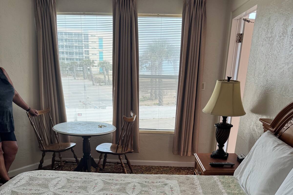 Habitación de hotel con cama, una mesa redonda, dos sillas, una lámpara y vistas al exterior.