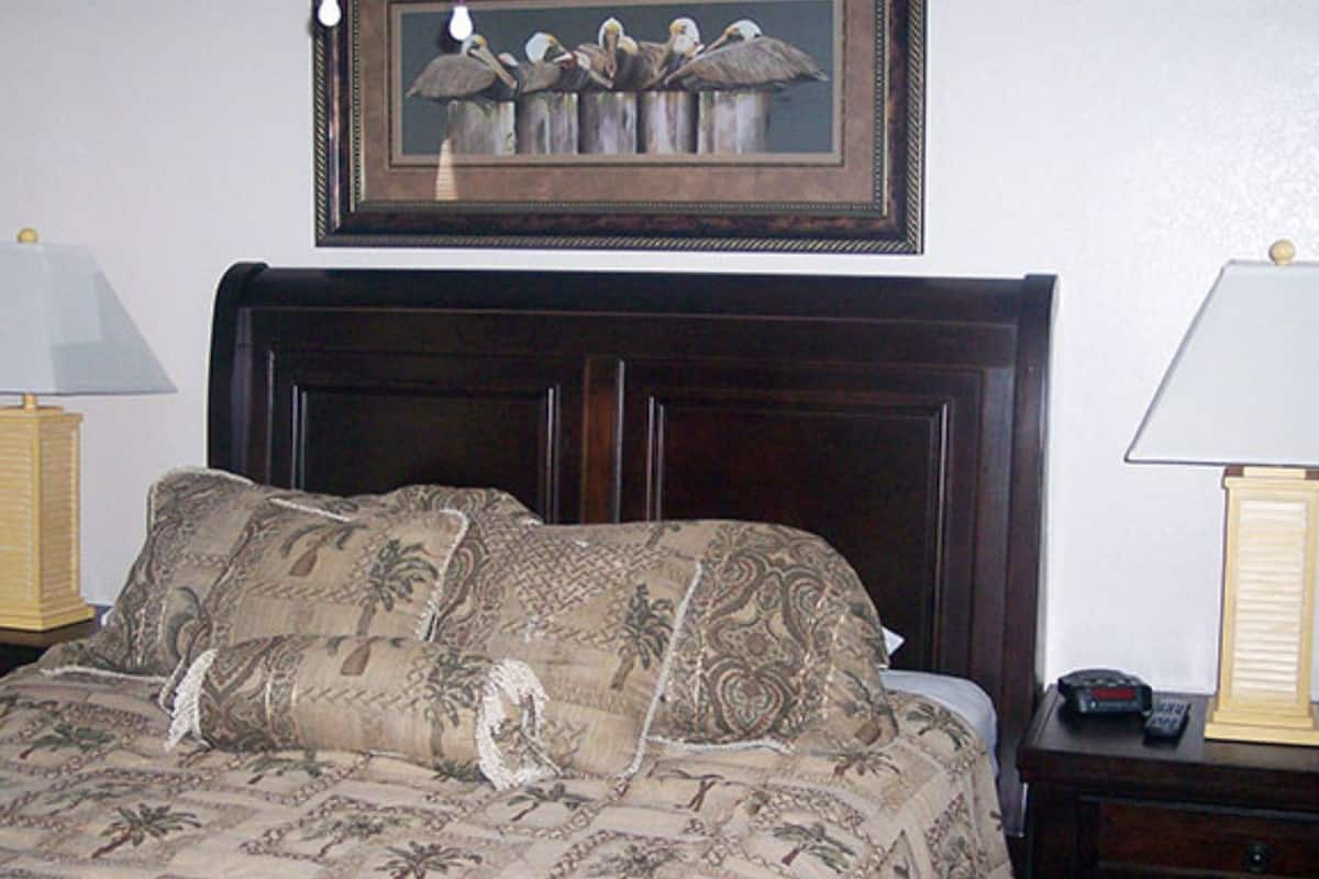 Una cama con una colcha estampada, una obra de arte enmarcada encima y lámparas de noche.