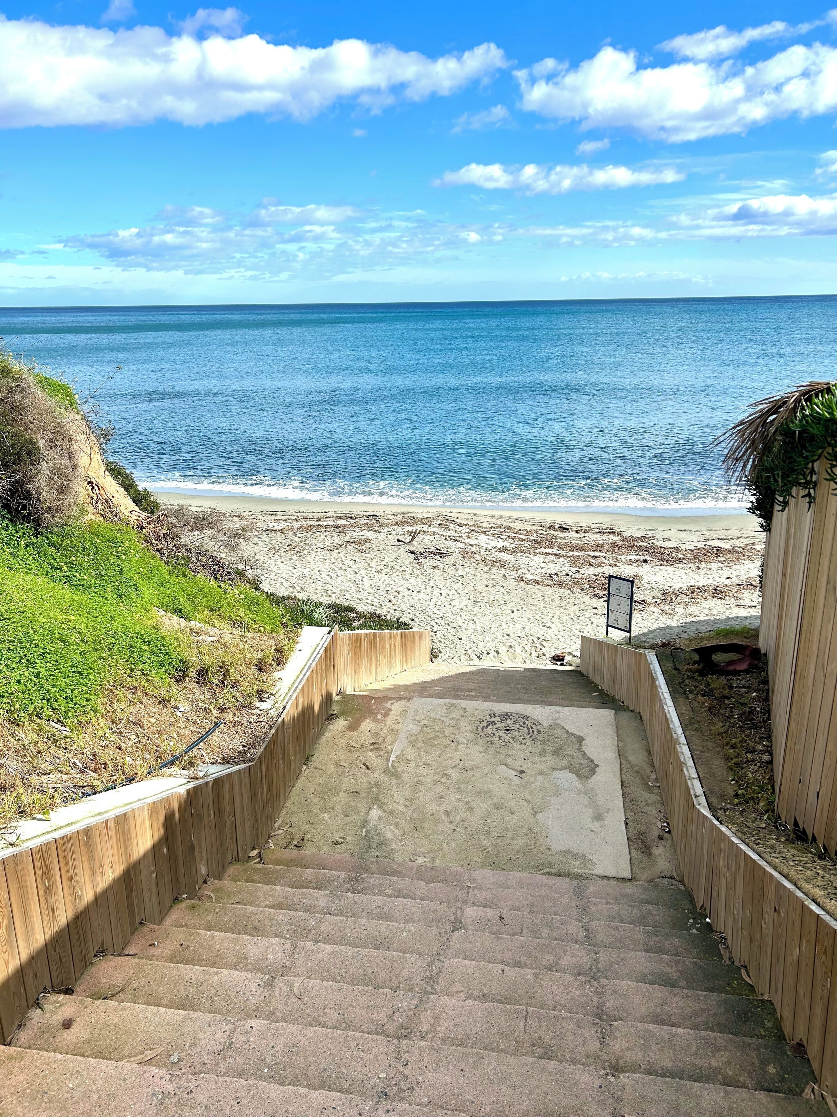 Una escalera que baja a una playa, flanqueada por una valla de madera a cada lado.