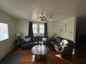 A living room with a ceiling fan, two leather sofas, a wooden coffee table, and a window with curtains.