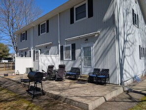 Ein zweistöckiges Haus mit überdachter Terrasse, Sitzgelegenheiten im Freien und einem Grill.
