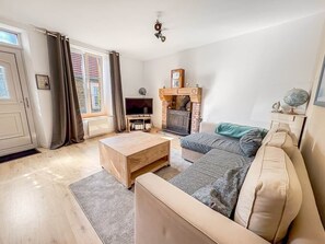 Ein Wohnzimmer mit einer Couch, Couchtisch, Fernseher, Kamin und einem Fenster mit Vorhängen.