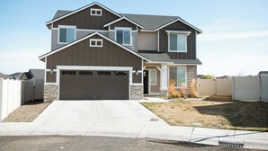 A two-story house with a garage, a front yard, and a white fence. - Spacious 5-bedroom house in lovely Twin Falls with AC (Twin Falls)