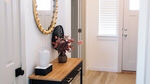 A hallway with a wooden console table, a mirror with a bead frame, a vase with flowers, and a trash can. - Spacious 5-bedroom house in lovely Twin Falls with AC (Twin Falls)