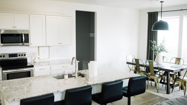 A modern kitchen with white cabinets, a built-in microwave, a stainless steel oven, and a marble island with bar stools. - Spacious 5-bedroom house in lovely Twin Falls with AC (Twin Falls)