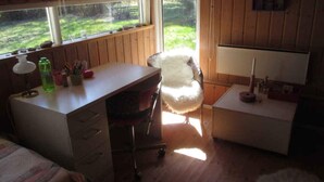 Una habitació petita i acollidora amb escriptori, cadira i una finestra gran.