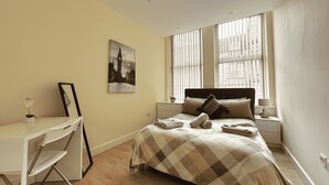 A bedroom with a bed, a desk, a chair, a window with blinds, and a wall-mounted picture. - Beautiful 2 bed Flat in City Centre (Sheffield)