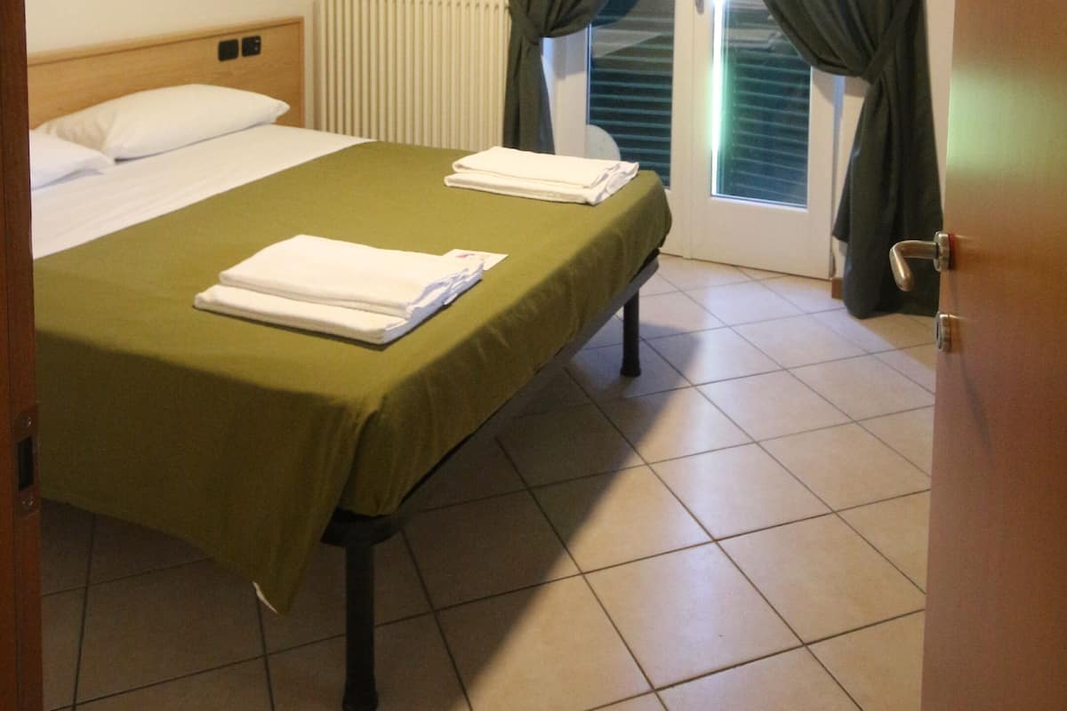A hotel room with a bed, a ceiling fan, a radiator, and a window with curtains.