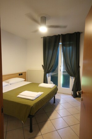 A hotel room with a bed, a ceiling fan, a radiator, and a window with curtains. - R&B Casa Wanda since 1999 (Riva del Garda)