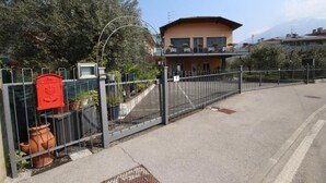 A gated entrance with a metal fence, a red mailbox, and a building with balconies in the background. - R&B Casa Wanda since 1999 (Riva del Garda)