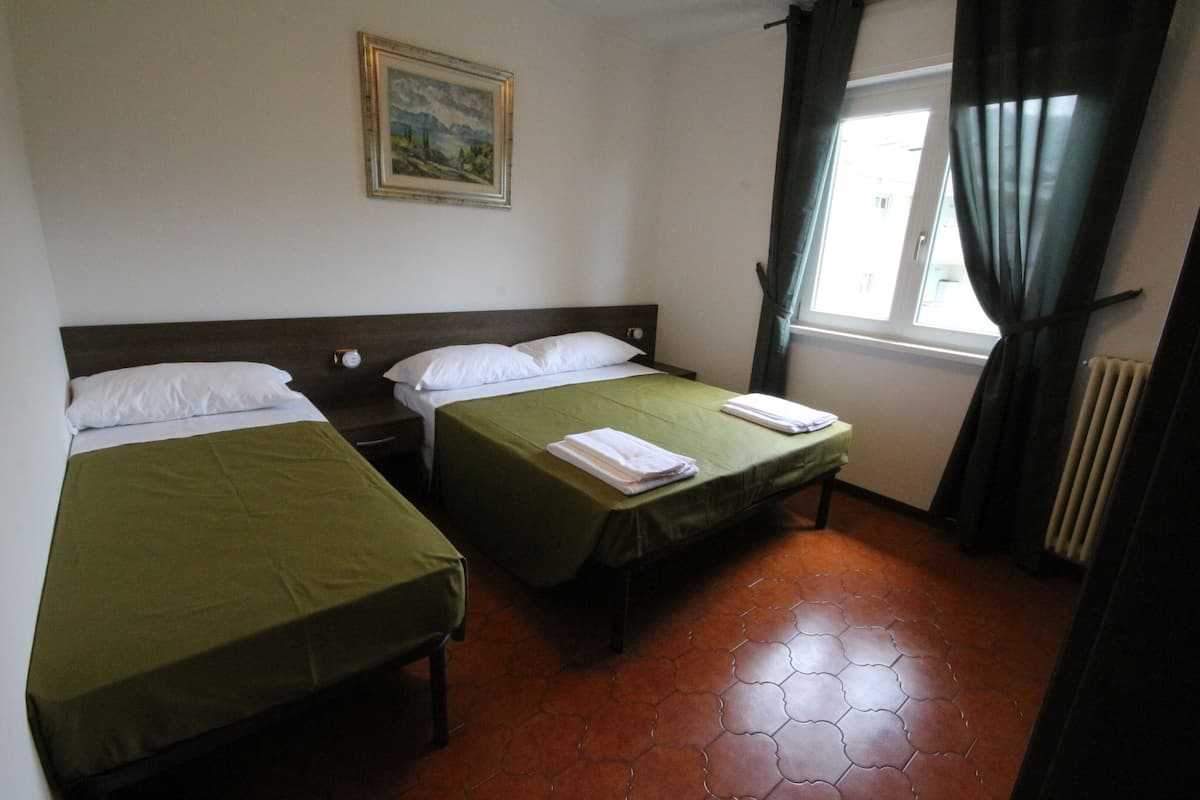 A room with two beds, a painting on the wall, a window with curtains, and a radiator.