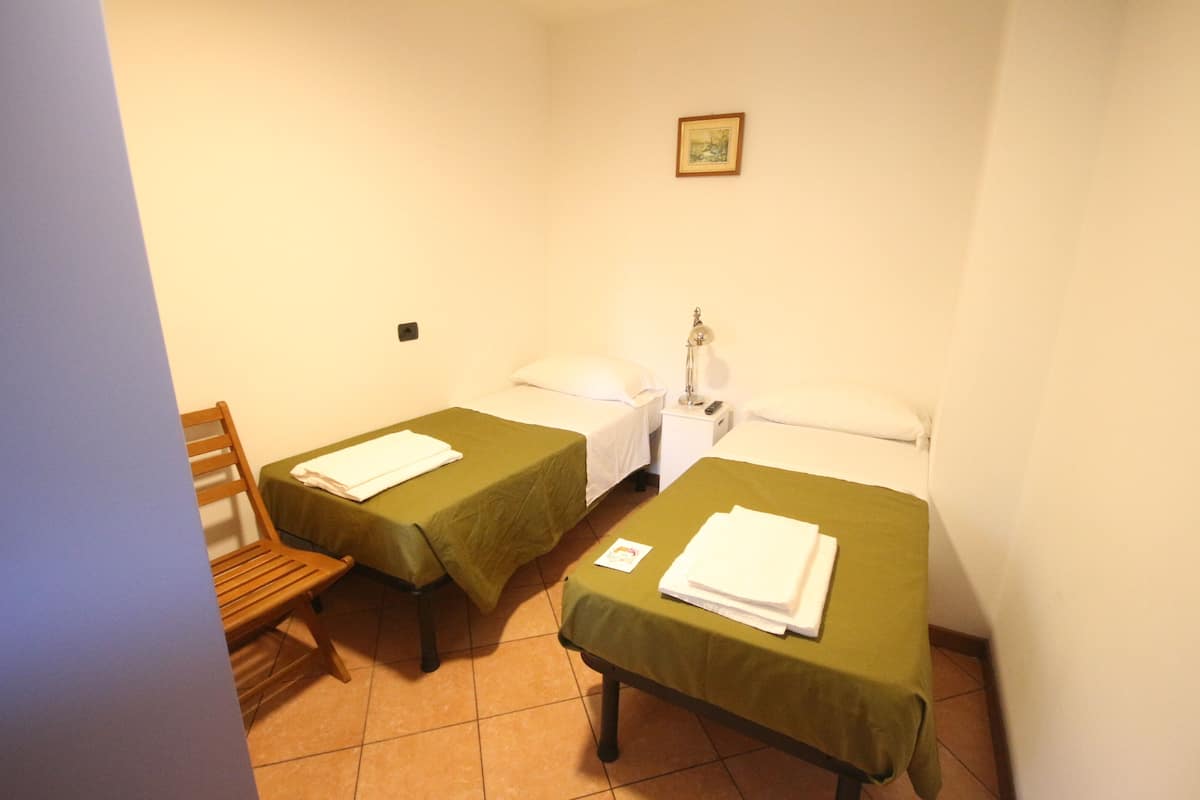 A room with two single beds, a wooden chair, a bedside table with a lamp, and a small framed picture on the wall.