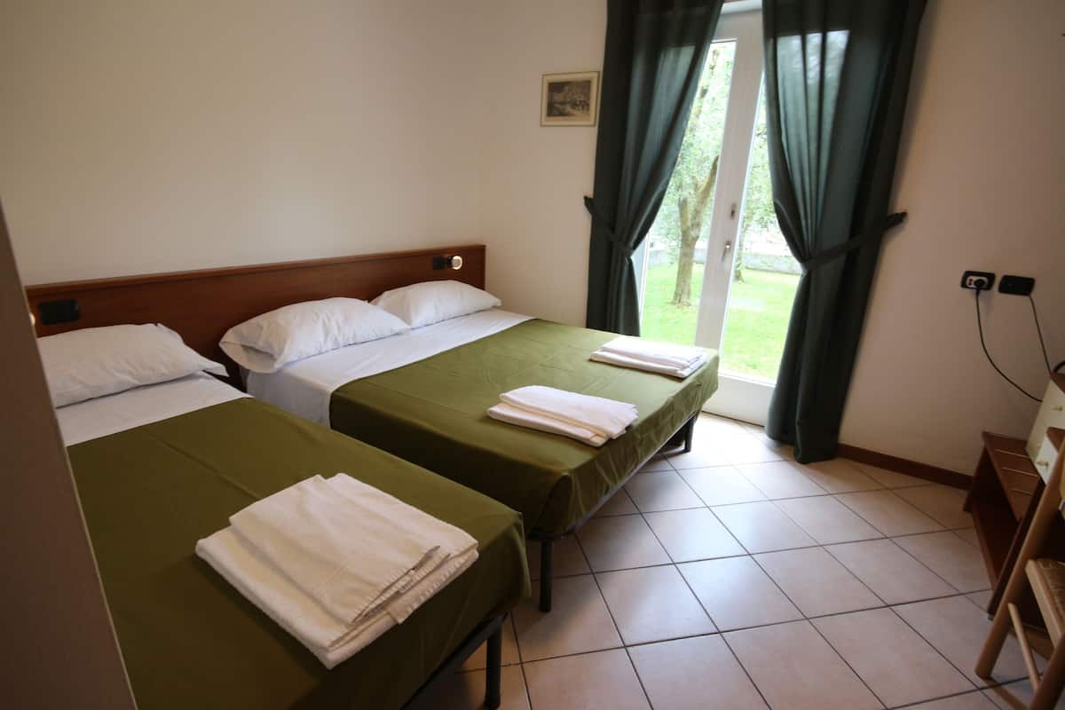 A hotel room with two beds, a wooden headboard, a window with curtains, and a tiled floor.