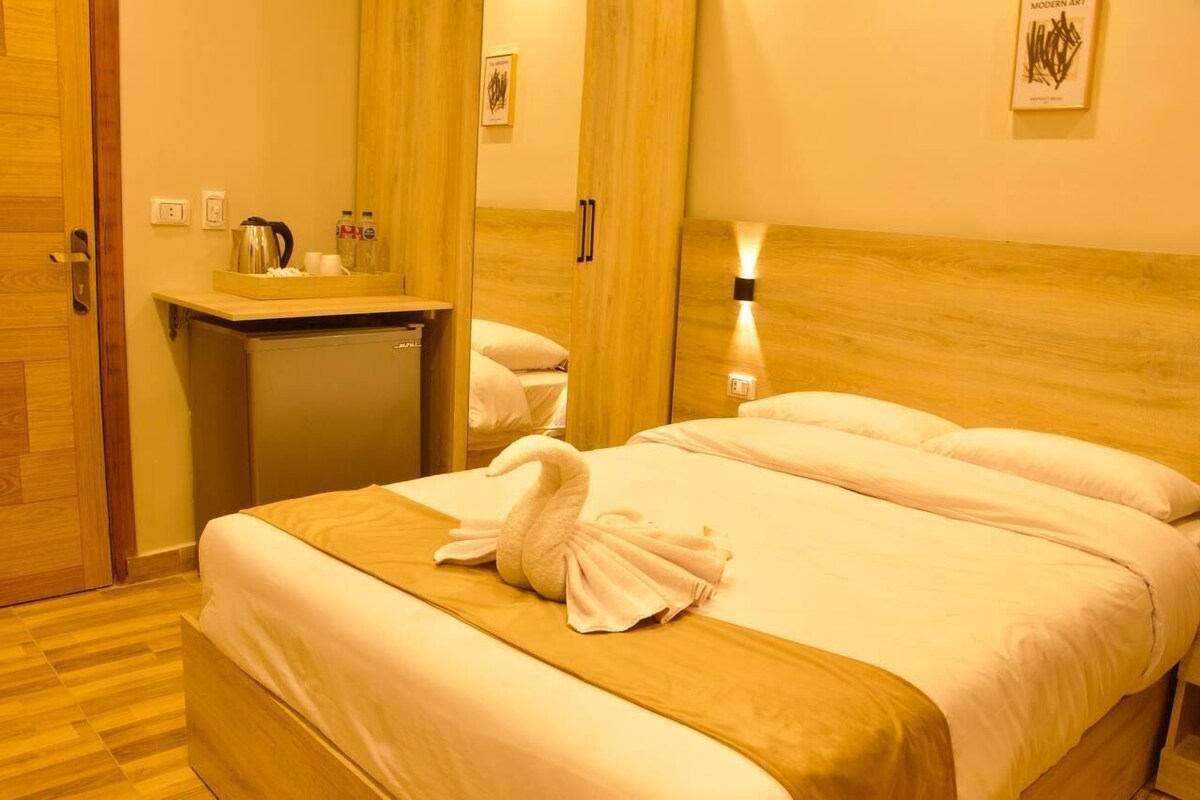 Una habitación de hotel con una cama, un escritorio pequeño, un espejo y una mesita de noche.