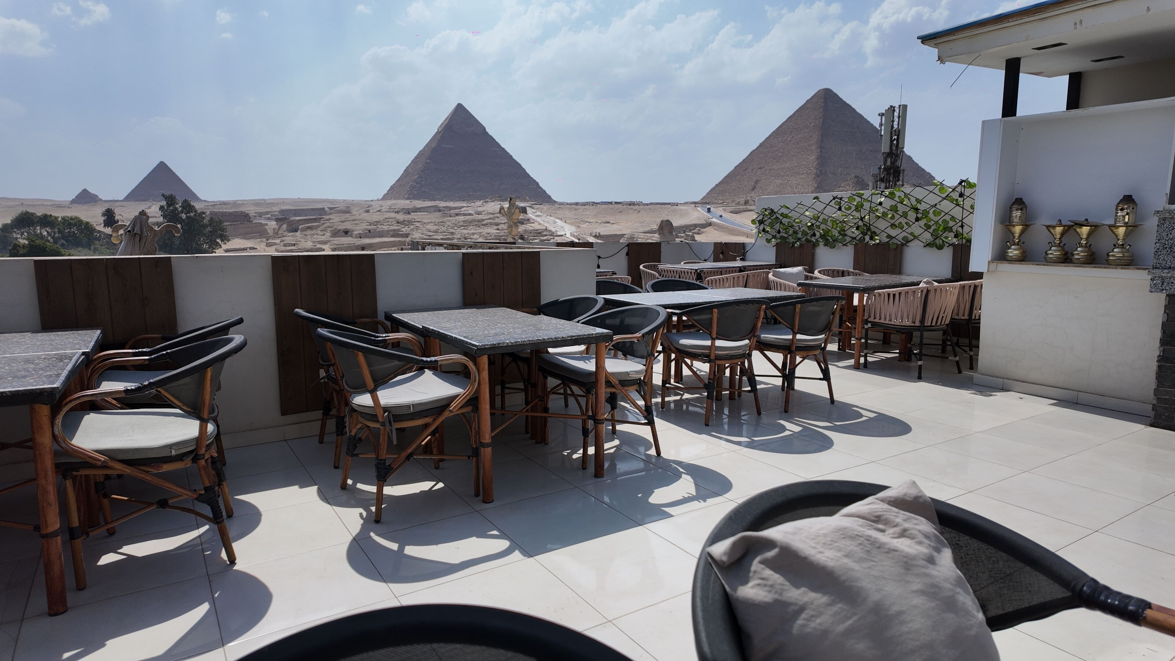 An outdoor seating area with tables and chairs, overlooking a desert landscape with pyramids.