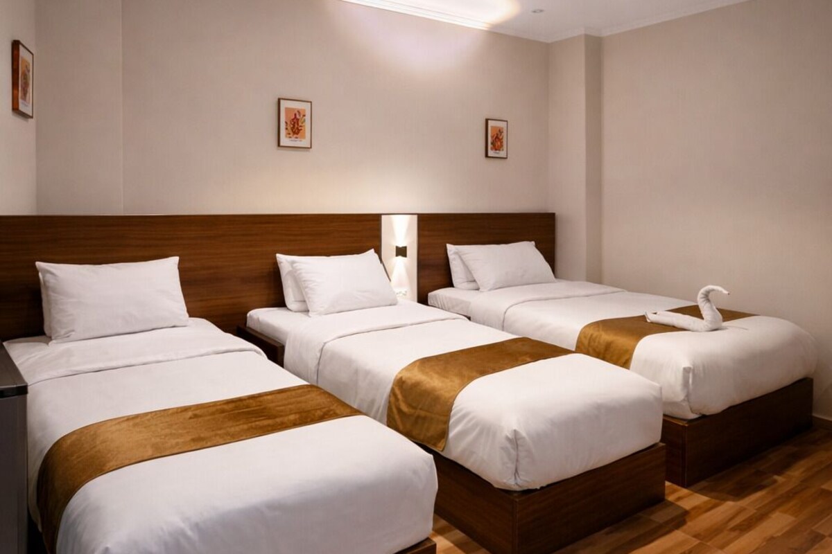 Una habitación de hotel con cuatro camas individuales, cabeceros de madera, ropa de cama blanca y piso de madera.