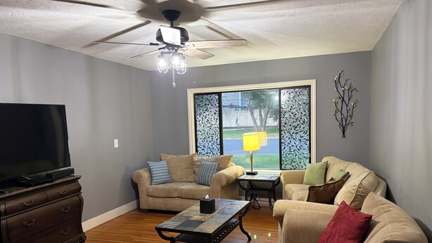 Una sala de estar con ventilador de techo, televisor de pantalla plana, sofá, sillón, mesa de centro y cómoda de madera.