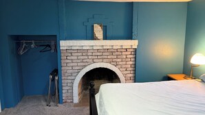 Un dormitorio con chimenea de ladrillo, una cama, una mesita de noche con lámpara y un perchero con colgadores.