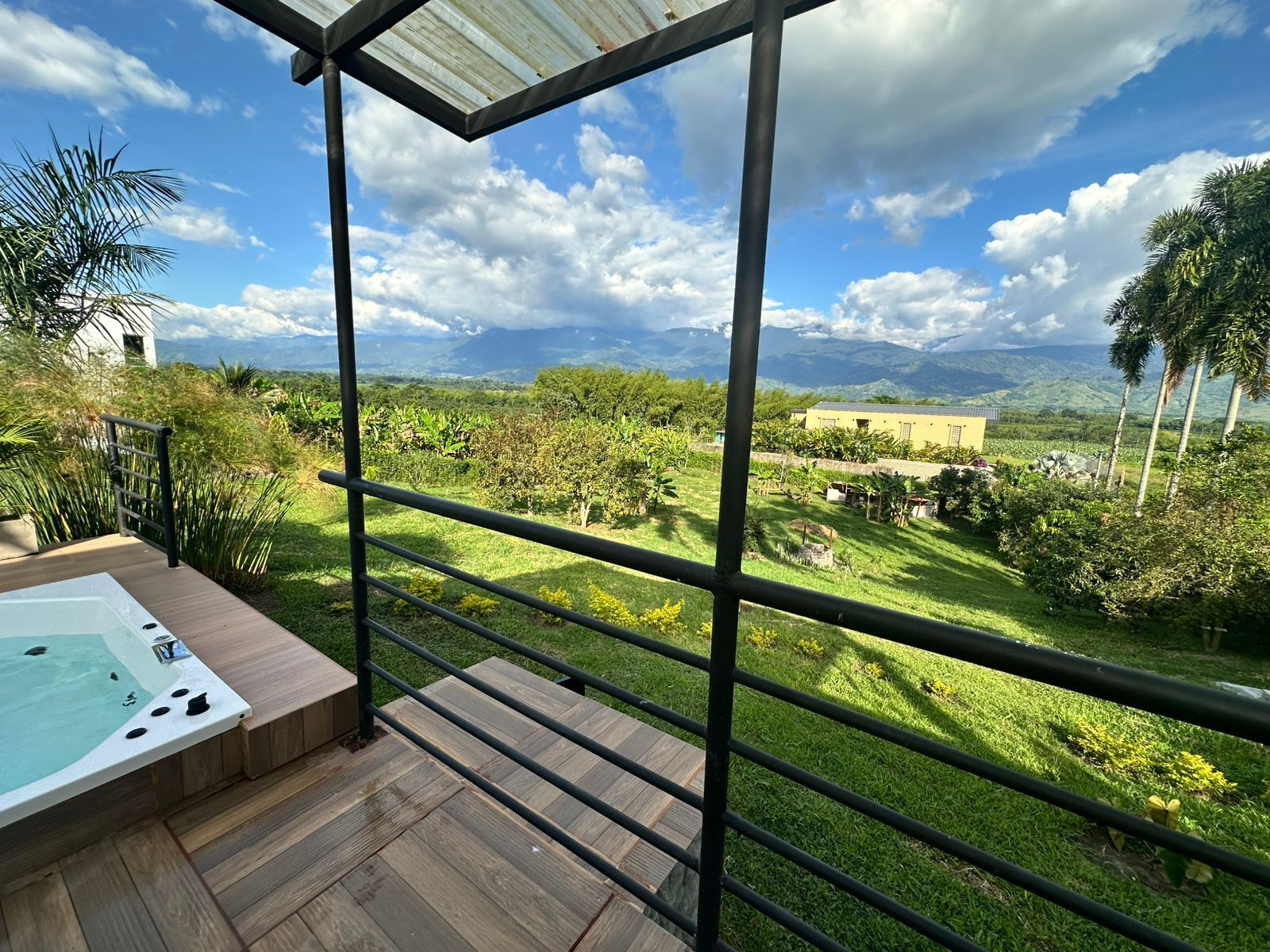 Un balcón con un jacuzzi, vistas a un paisaje exuberante y una cadena montañosa en la distancia.