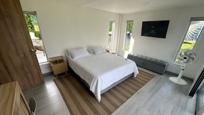 Un dormitorio moderno con cama, mesitas de noche, un banco, un ventilador y una televisión.