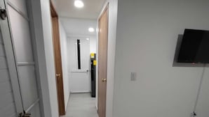 Un pasillo con paredes blancas, piso de baldosas y un televisor de pantalla plana montado en la pared.