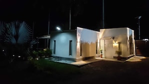 Un edificio moderno con techo plano, dos puertas visibles y un pequeño jardín con una palmera.