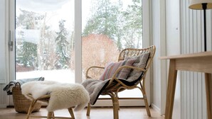 A wicker chair with a cushion, a fluffy white stool, and a table with a lamp. - 4 Star Holiday Home in Nykobing Sj (Nykobing Sjaelland)
