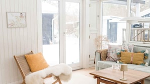 A cozy living room with a wooden chair, a white furry throw, a light-colored sofa with colorful pillows, a wooden coffee table, and a large window. - 4 Star Holiday Home in Nykobing Sj (Nykobing Sjaelland)