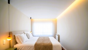 A hotel room with a bed, bedside lamp, and a window with curtains. - Casa Marmite Sea View (Matosinhos)