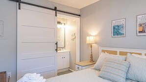 Een slaapkamer met een bed, een nachtkastje, een lamp, een schuifdeur en een muur met ingelijste foto's.