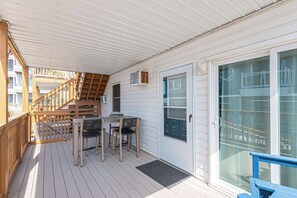 A covered outdoor deck with a wooden staircase, a table with chairs, and a sliding glass door. - Bayview Condo Short Walk to Beach (Ocean City)