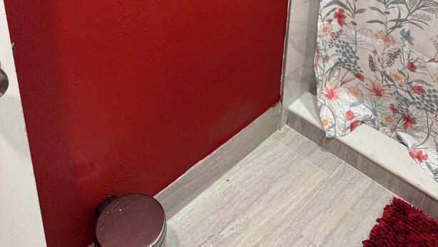 Una parete rossa, una tenda da doccia con motivi floreali e un tappeto rosso.
