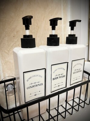 Three bottles of conditioner, body wash, and shampoo on a metal rack. - Modern Studio With Free Parking Near City Airport and ExCel (London)