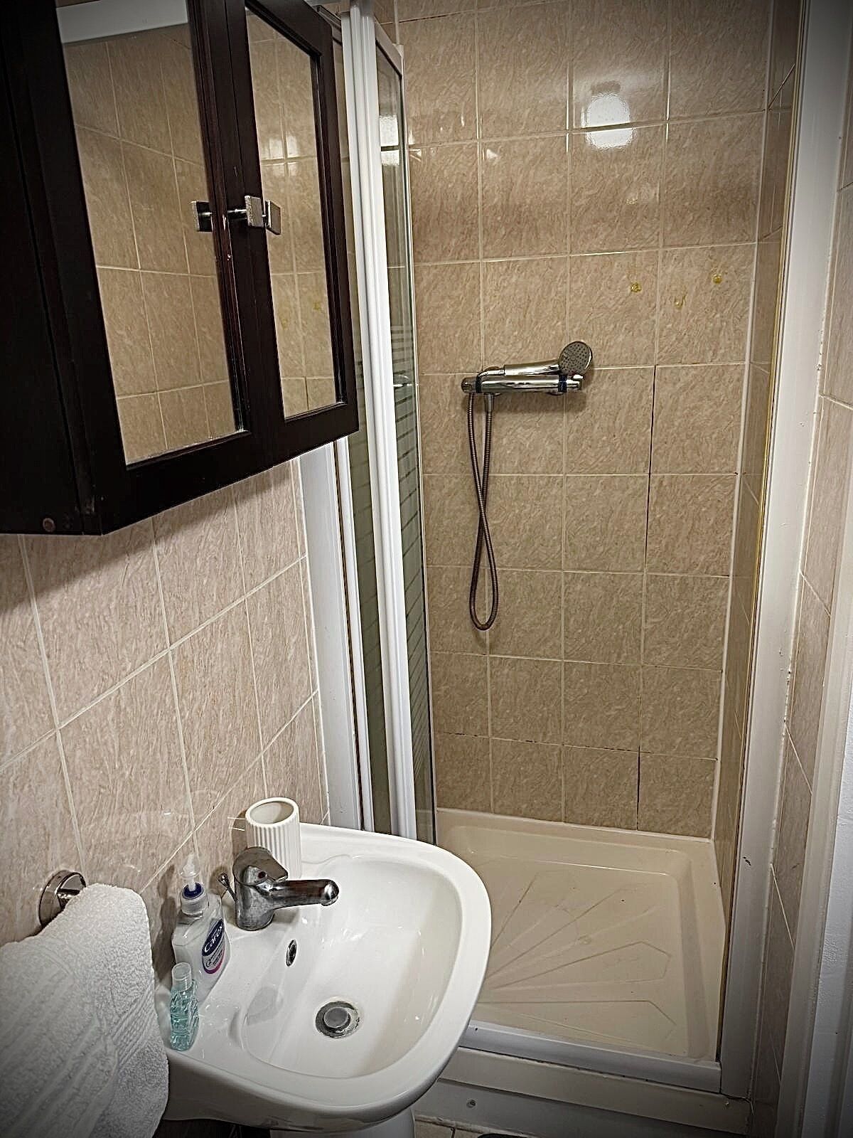 Une salle de bain avec une douche, un lavabo, un miroir et une serviette.