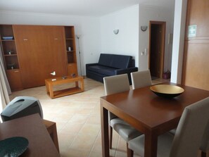 A living room with a sofa, a coffee table, and a dining table with chairs. - Quinta Velha Garden Pool Flat 116 (Tavira)