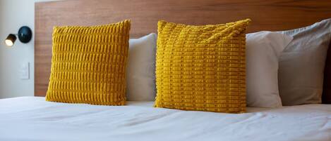 Una cama con ropa de cama blanca, dos almohadas amarillas con textura y un cabecero de madera.