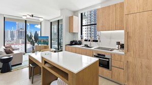 A modern kitchen with wooden cabinets, a white countertop, and a large window offering a city view. - 2BR/2BA | Pool  |  8 Min to Port of Miami Cruises (Miami)