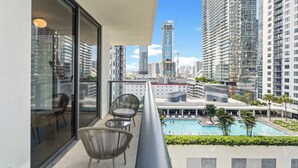 A balcony with a view of a cityscape, including high-rise buildings and a swimming pool. - 2BR/2BA | Pool  |  8 Min to Port of Miami Cruises (Miami)