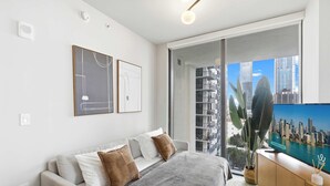 A modern bedroom with a large bed, a TV, and a balcony with a city view. - 2BR/2BA | Pool  |  8 Min to Port of Miami Cruises (Miami)
