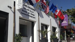 Una oficina de cambio de divisas con varias banderas, plantas en macetas y un cielo despejado.