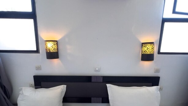 Una habitación de hotel con una cama, dos mesitas de noche y dos lámparas de pared.