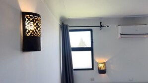 Habitación de hotel con cama, ventana con cortinas, aire acondicionado de pared y una lámpara decorativa en la pared.