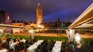 Un restaurante con mesas dispuestas para comer, vista a una torre y un cartel del hotel.