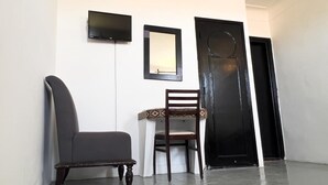 Un pasillo con una silla oscura, una silla blanca, un espejo enmarcado y una puerta negra.