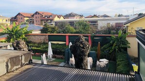 Ein Dachgarten mit Topfpflanzen, Gartenmöbeln und Blick auf Wohnhäuser.