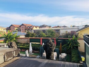 A rooftop garden with potted plants, outdoor furniture, and a view of residential buildings. - LINGUA ITALIANO (Rho)