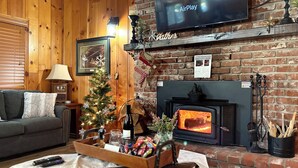 Ein gemütliches Wohnzimmer mit Kamin, Fernseher, Weihnachtstannen und Couchtisch.